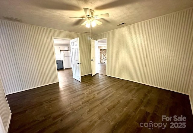 empty room featuring ceiling fan, dark wood-type flooring, visible vents, and wallpapered walls