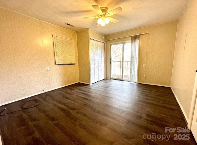 empty room with dark wood-style flooring, a ceiling fan, baseboards, visible vents, and wallpapered walls