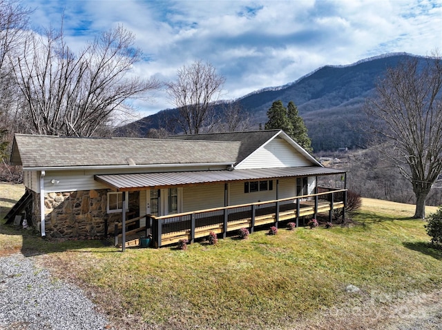 view of front of house featuring stone siding, a shingled roof, a mountain view, and a front lawn