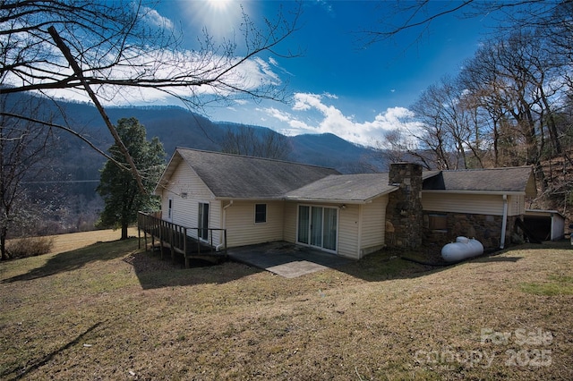 back of property with a chimney, a mountain view, and a yard