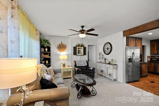 living room with ceiling fan, beam ceiling, carpet, and a textured ceiling