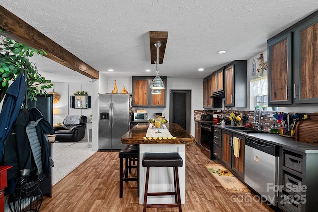 kitchen featuring a breakfast bar, a center island, hanging light fixtures, appliances with stainless steel finishes, and hardwood / wood-style flooring