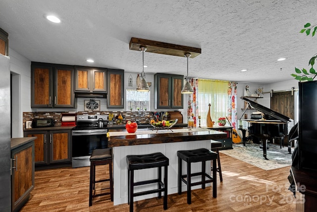 kitchen featuring stainless steel electric stove, a breakfast bar, light hardwood / wood-style floors, and hanging light fixtures