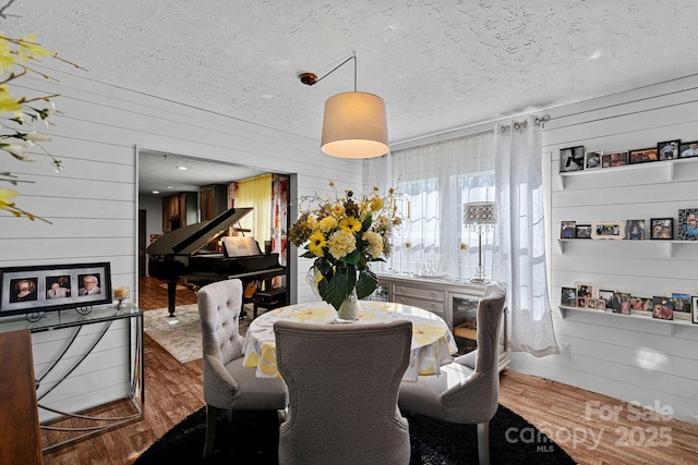 dining room with hardwood / wood-style flooring, a textured ceiling, and wood walls