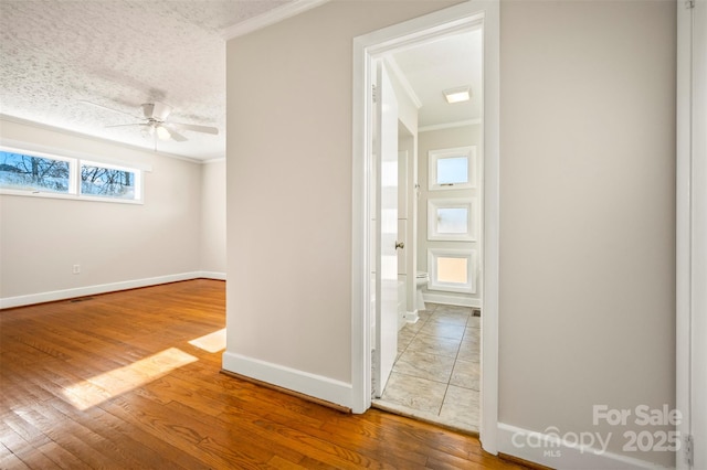 corridor with a textured ceiling, ornamental molding, and hardwood / wood-style flooring