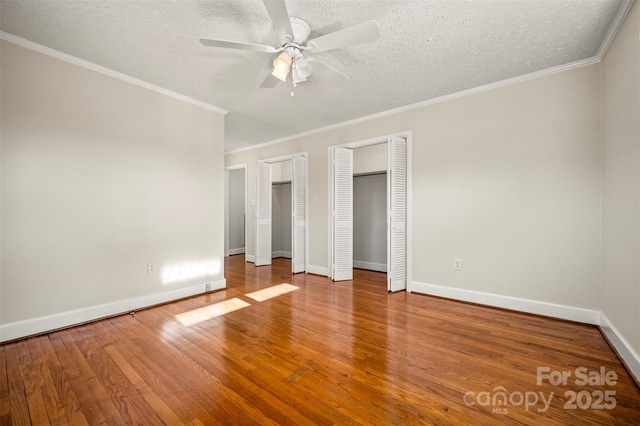 unfurnished bedroom with ceiling fan, hardwood / wood-style floors, two closets, a textured ceiling, and ornamental molding