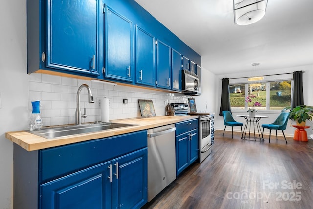 kitchen featuring appliances with stainless steel finishes, sink, decorative backsplash, blue cabinets, and wood counters