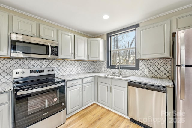 kitchen featuring sink, tasteful backsplash, appliances with stainless steel finishes, light stone countertops, and light hardwood / wood-style floors