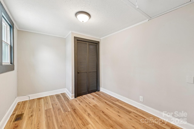 unfurnished bedroom with wood-type flooring, a textured ceiling, crown molding, and a closet