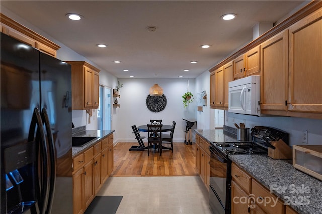 kitchen featuring dark stone counters, light wood-type flooring, and black appliances