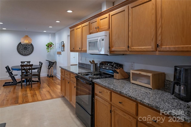 kitchen featuring black range with electric cooktop, light hardwood / wood-style flooring, and dark stone countertops