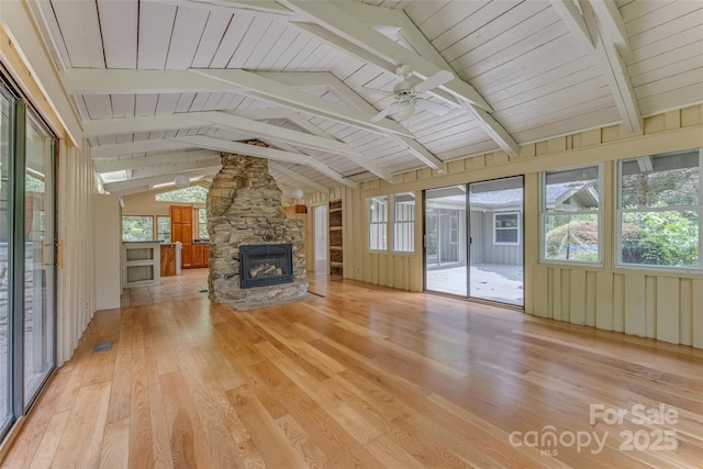 unfurnished living room featuring a stone fireplace, light hardwood / wood-style floors, lofted ceiling with beams, ceiling fan, and wooden ceiling