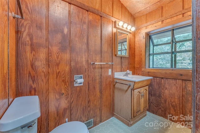 bathroom with toilet, vanity, tile patterned floors, and wood walls