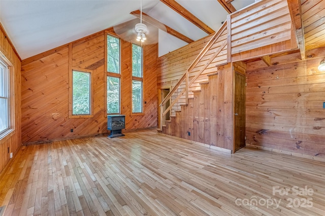 unfurnished living room with vaulted ceiling, a wood stove, and wood walls