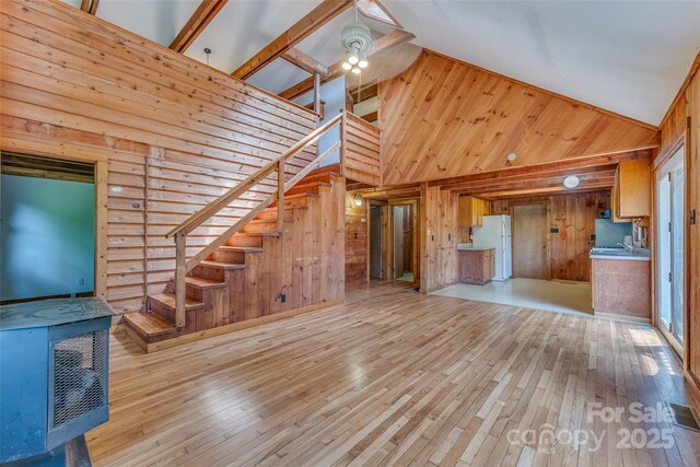 unfurnished living room with high vaulted ceiling, light hardwood / wood-style floors, and wood walls