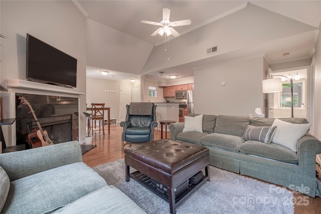 living room featuring visible vents, crown molding, vaulted ceiling, light wood-style flooring, and a fireplace