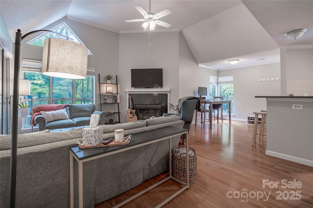 living area with wood finished floors, baseboards, a fireplace, ceiling fan, and crown molding