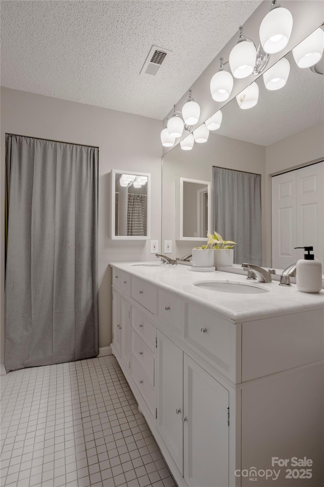 full bath with visible vents, a sink, a textured ceiling, tile patterned flooring, and double vanity