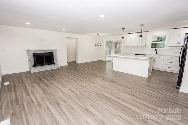 kitchen with pendant lighting, a center island, black refrigerator, white cabinetry, and a brick fireplace