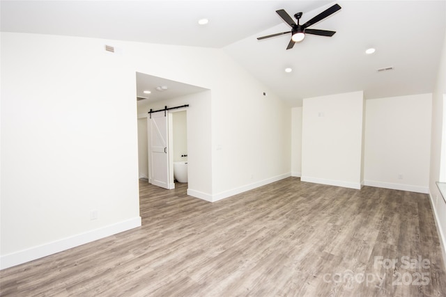 unfurnished room with ceiling fan, a barn door, light hardwood / wood-style flooring, and lofted ceiling