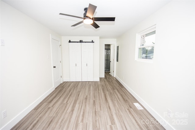 unfurnished bedroom with ceiling fan, light hardwood / wood-style flooring, and a barn door