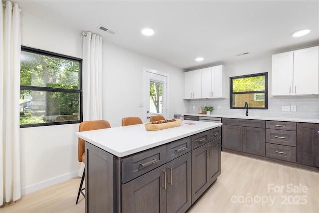 kitchen with tasteful backsplash, dark brown cabinetry, white cabinets, a breakfast bar, and sink