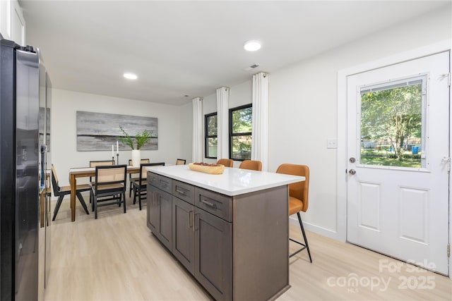 kitchen with stainless steel fridge, a breakfast bar area, light wood-type flooring, dark brown cabinets, and a center island