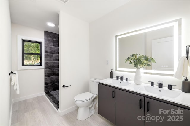 bathroom with toilet, tiled shower, and vanity