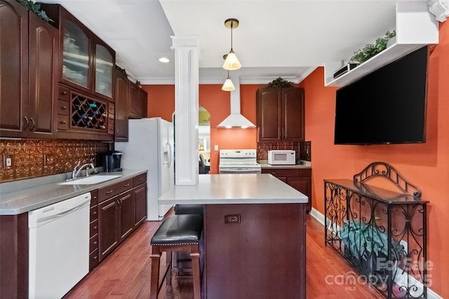 kitchen with white appliances, decorative light fixtures, wall chimney range hood, tasteful backsplash, and sink