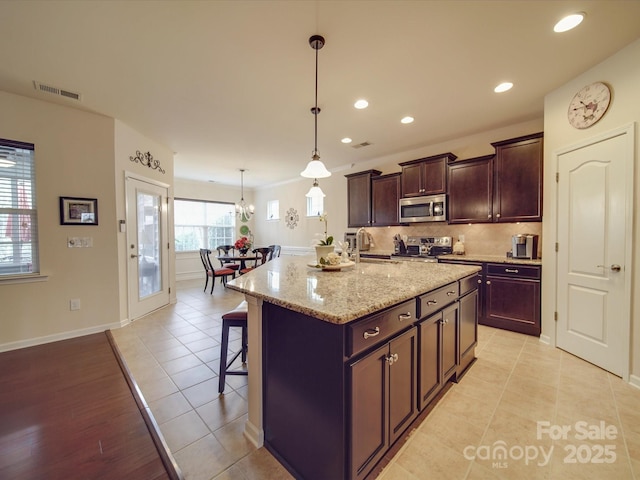 kitchen with a breakfast bar, decorative light fixtures, an island with sink, stainless steel appliances, and light stone countertops