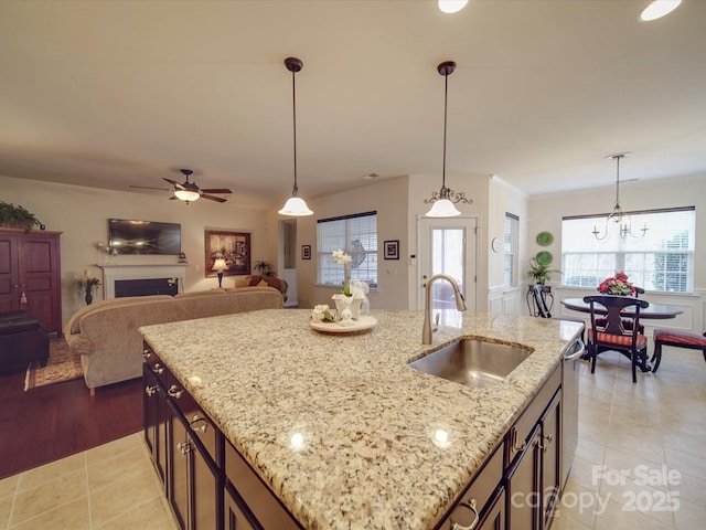 kitchen with light stone counters, a kitchen island with sink, sink, and hanging light fixtures