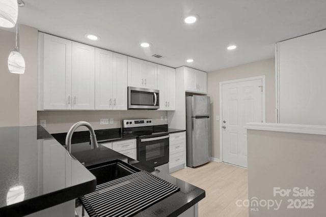 kitchen featuring pendant lighting, white cabinets, appliances with stainless steel finishes, sink, and light hardwood / wood-style flooring