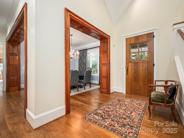 entryway with hardwood / wood-style floors, vaulted ceiling, crown molding, and an inviting chandelier