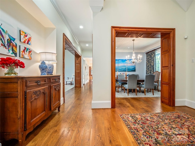 hall with an inviting chandelier, ornamental molding, and hardwood / wood-style flooring