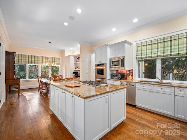 kitchen featuring light stone countertops, a center island, decorative light fixtures, white cabinetry, and stainless steel appliances