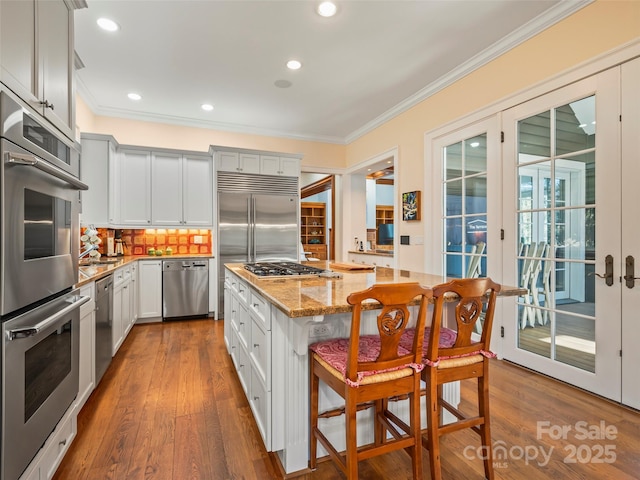 kitchen featuring light stone countertops, a center island, stainless steel appliances, decorative backsplash, and a breakfast bar area