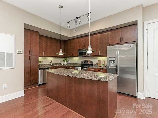 kitchen featuring a kitchen island, appliances with stainless steel finishes, decorative light fixtures, dark stone counters, and dark brown cabinets