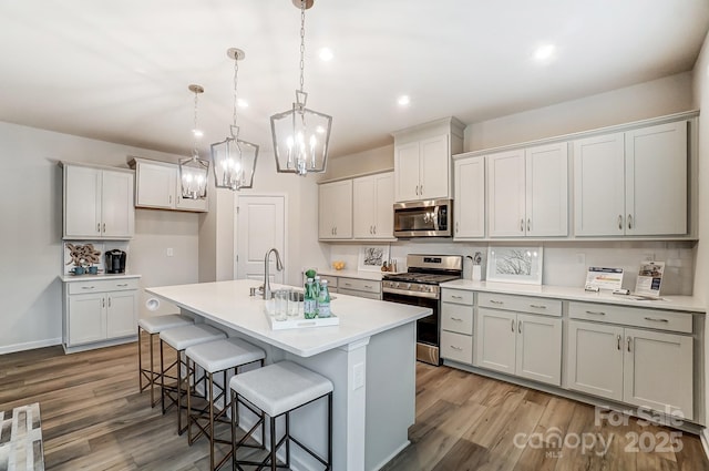 kitchen featuring pendant lighting, stainless steel appliances, light hardwood / wood-style floors, a kitchen breakfast bar, and a center island with sink