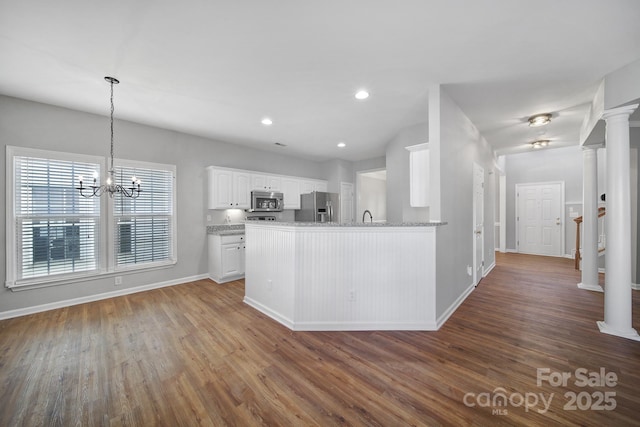 kitchen with dark hardwood / wood-style floors, decorative columns, white cabinetry, kitchen peninsula, and stainless steel appliances