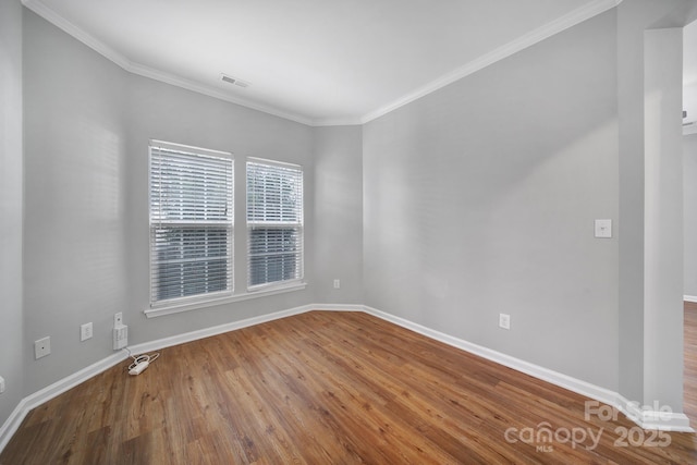 empty room with crown molding, wood finished floors, visible vents, and baseboards