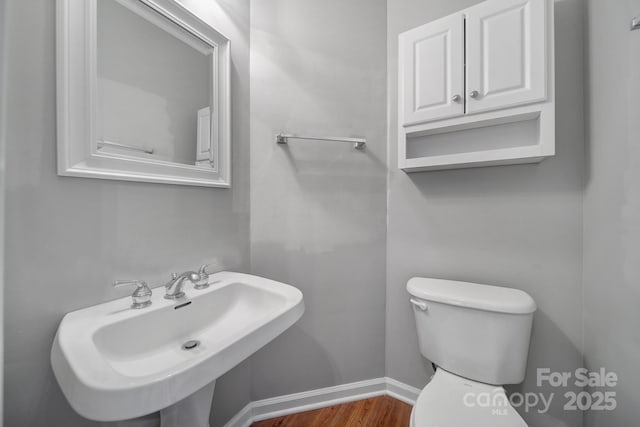 half bathroom featuring toilet, baseboards, a sink, and wood finished floors