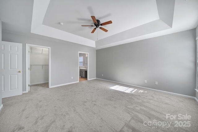 unfurnished bedroom featuring a walk in closet, connected bathroom, light colored carpet, and a tray ceiling