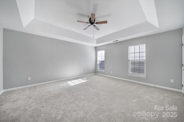 empty room featuring ceiling fan, a tray ceiling, carpet flooring, and baseboards