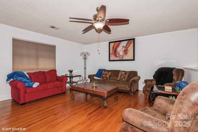 living room featuring hardwood / wood-style flooring, ceiling fan, and a textured ceiling