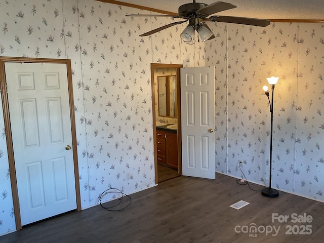 unfurnished bedroom with ceiling fan, ensuite bathroom, a textured ceiling, and dark hardwood / wood-style flooring