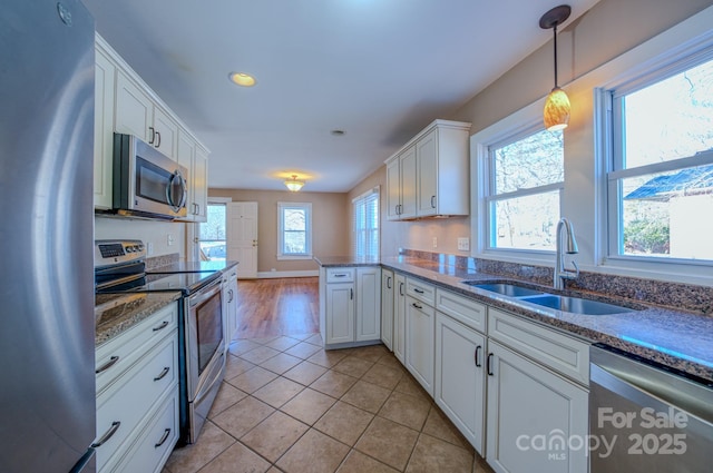 kitchen with white cabinetry, kitchen peninsula, appliances with stainless steel finishes, hanging light fixtures, and sink