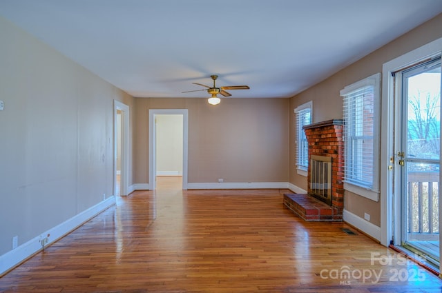 unfurnished living room with ceiling fan, light wood-type flooring, a brick fireplace, and a wealth of natural light