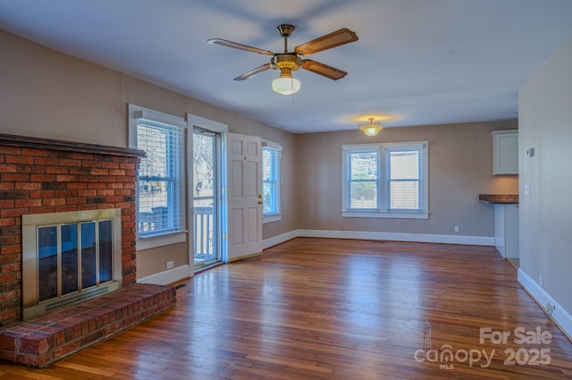 unfurnished living room featuring ceiling fan, dark hardwood / wood-style floors, plenty of natural light, and a brick fireplace