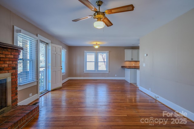 unfurnished living room featuring ceiling fan, a fireplace, and dark hardwood / wood-style floors