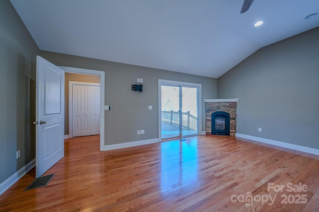 unfurnished living room featuring lofted ceiling, ceiling fan, a stone fireplace, and light hardwood / wood-style floors